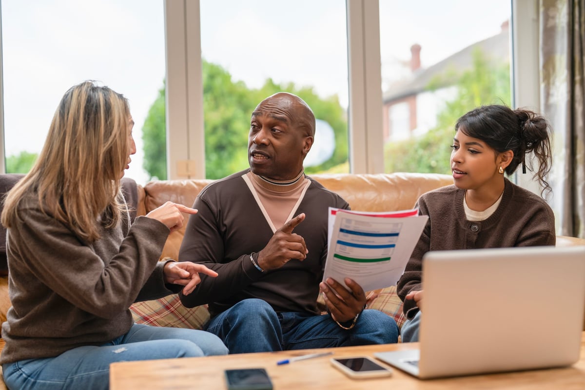 Three people from different generations gathered at home reviewing documents and discussing plans together in a warm, candid setting